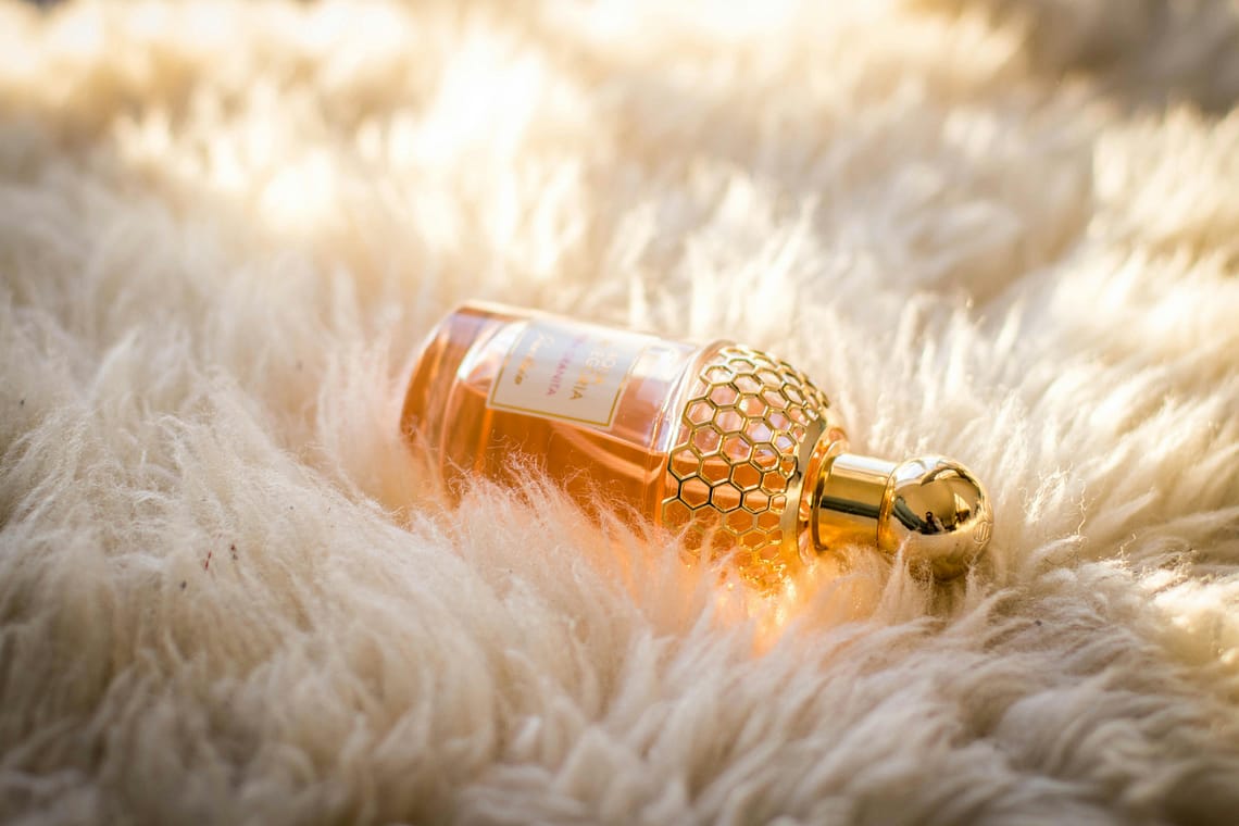 Trendi parfumov leta 2025 32 Elegant perfume bottle with gold details resting on fluffy white fur, capturing luxury and glamour.