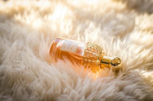Elegant perfume bottle with gold details resting on fluffy white fur, capturing luxury and glamour.